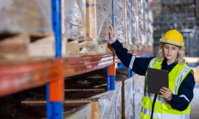 Woman in a high vis vest inspect inventory stock in a warehouse.