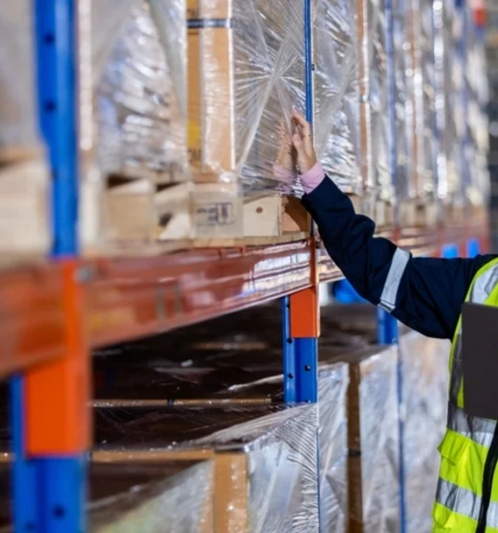 Woman in a high vis vest inspect inventory stock in a warehouse.