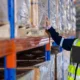 Woman in a high vis vest inspect inventory stock in a warehouse.