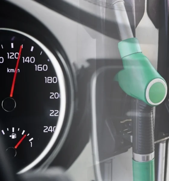 Fuel pomp nozzles beside a car dashboard speedometer showing a full petrol
