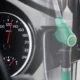 Fuel pomp nozzles beside a car dashboard speedometer showing a full petrol