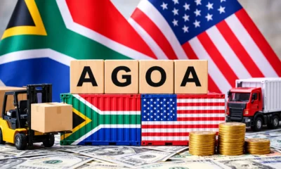 A South African and US flag sitting on a desk with toy freight vehicles transporting goods. In the centre, lies two shipping containers painted with a South African and US flag with letters on top spelling AGOA.