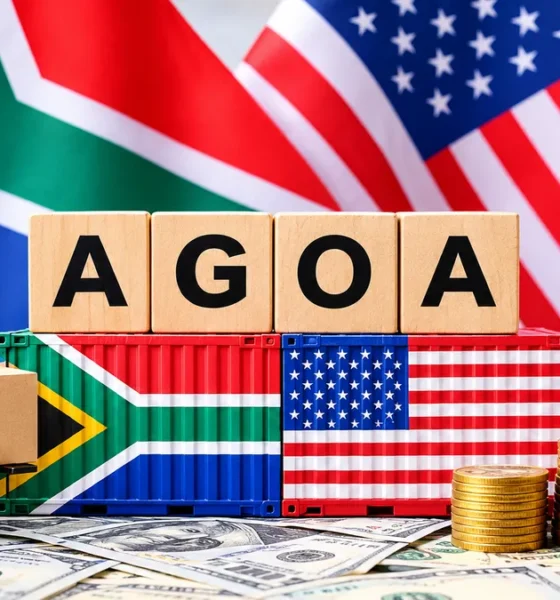 A South African and US flag sitting on a desk with toy freight vehicles transporting goods. In the centre, lies two shipping containers painted with a South African and US flag with letters on top spelling AGOA.