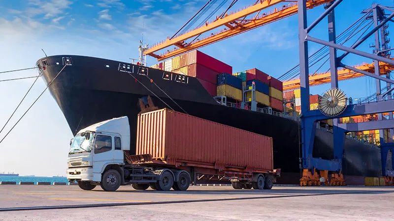 Freight ship docked in a harbour with a freight truck preparing to pick up the cargo.