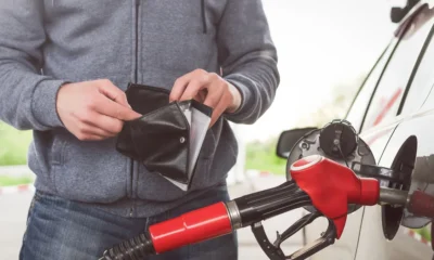 Man fulling up with his car with petrol while opening his wallet.