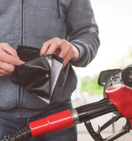 Man fulling up with his car with petrol while opening his wallet.
