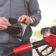 Man fulling up with his car with petrol while opening his wallet.