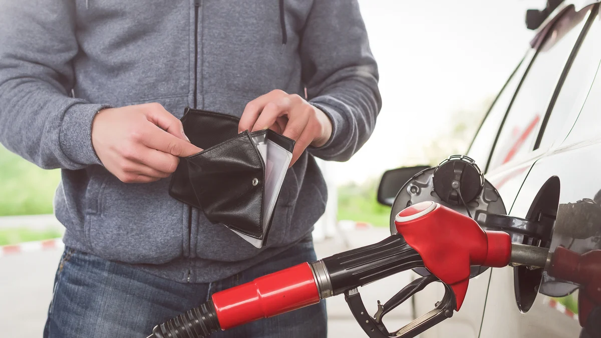 Man fulling up with his car with petrol while opening his wallet.